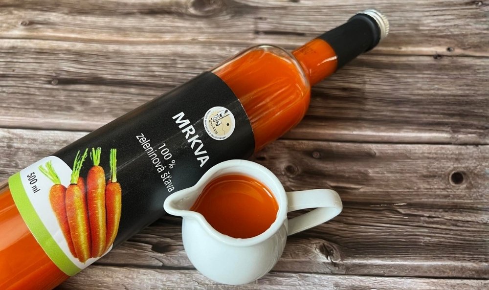 Fľaša mrkvovej zeleninovej šťavy a malý biely džbánik s nápojom na drevenom stole