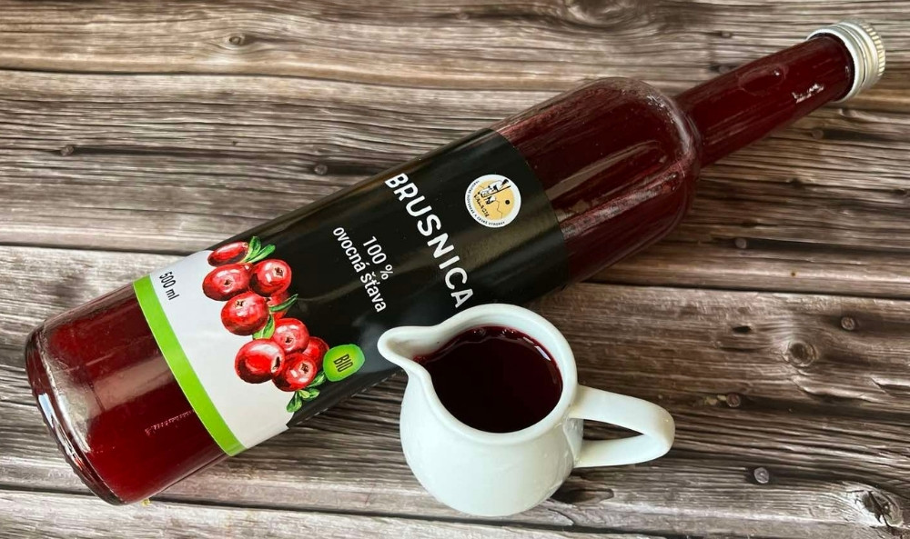 Fľaša brusnicovej ovocnej šťavy a malý biely džbánik s nápojom na drevenom stole