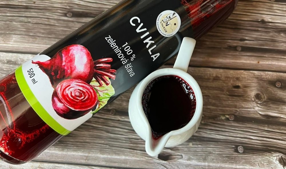 Fľaša cviklovej zeleninovej šťavy a malý biely džbánik s nápojom na drevenom stole