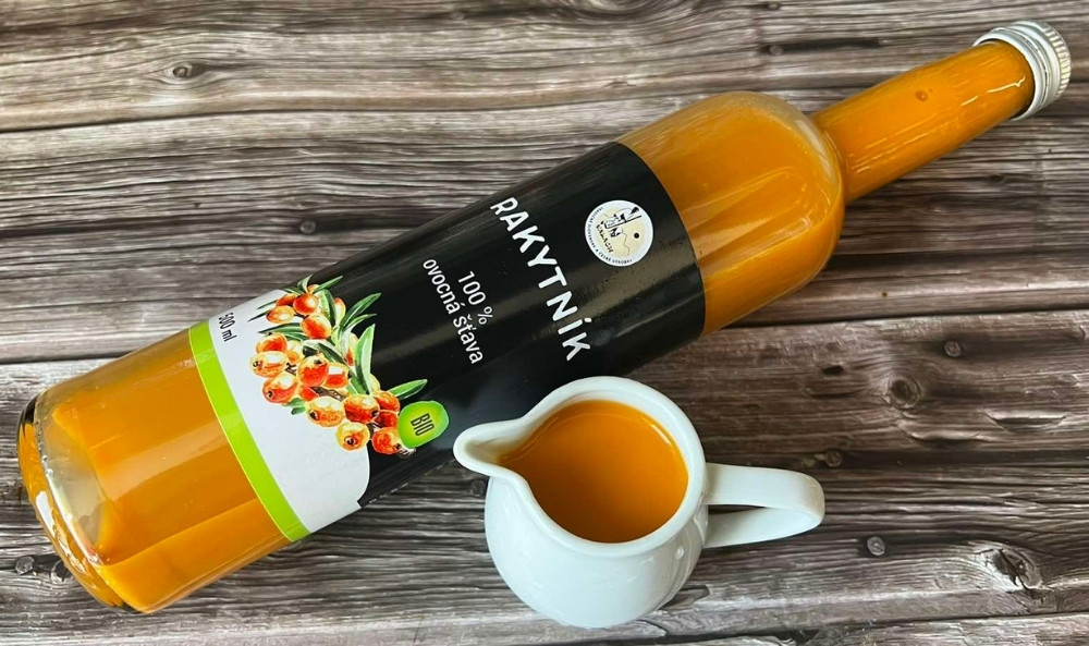 Fľaša rakytníkovej ovocnej šťavy a malý biely džbánik s nápojom na drevenom stole