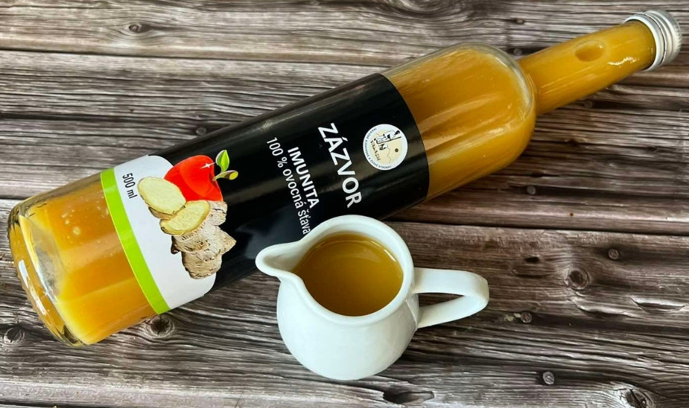 Fľaša zázvorovej ovocnej šťavy a malý biely džbánik s nápojom na drevenom stole