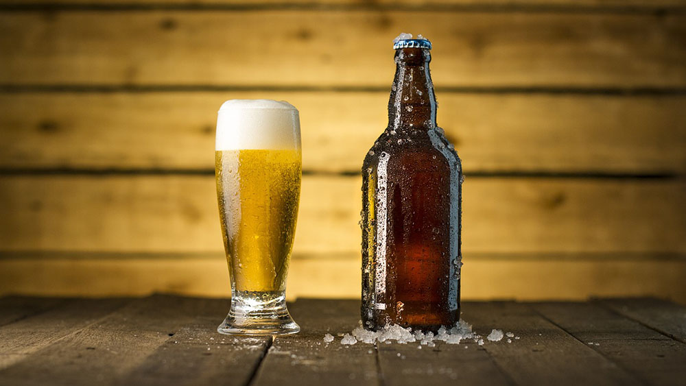 detail piva v sklenenom pohári a pivovej fľašky na drevenom podklade