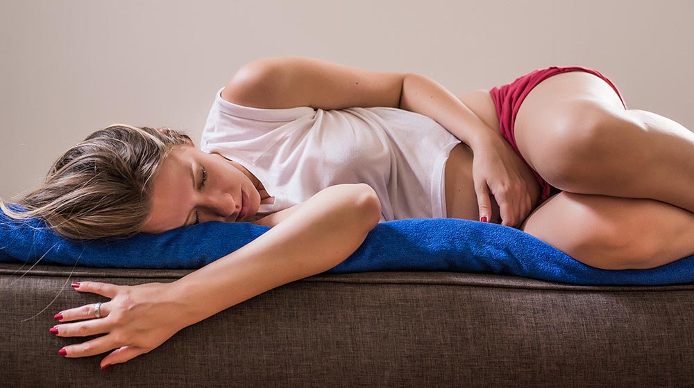 Žena ležiaca na modrej deke s menštruačnou bolesťou