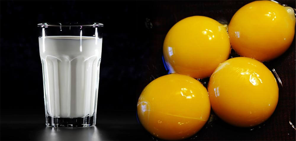 pohár mlieka a detail vaječných žĺtkov na čiernom podklade