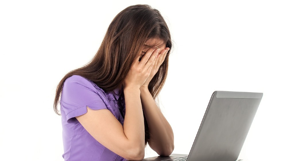 unavená žena pracujúca na počítači držiaca si rukami tvár